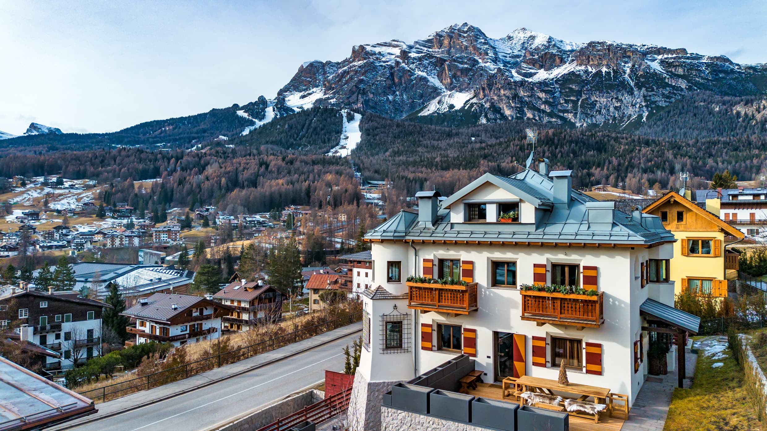 Vista aerea di Villa Il Castelletto a Cortina d'Ampezzo, scuri tirolesi rossi, torretta e tetto in zinco con le Dolomiti innevate sullo sfondo