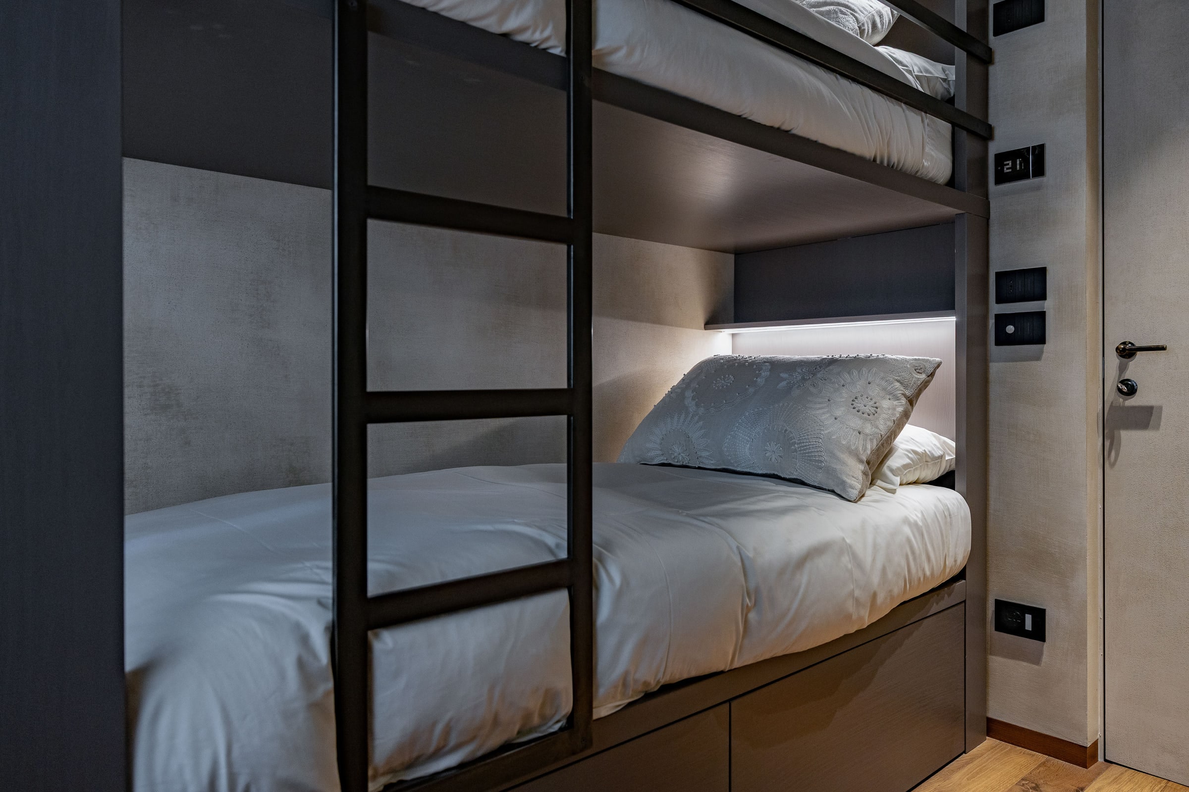Camera con letto a castello in metallo scuro e cuscini ricamati, scala e luce di lettura