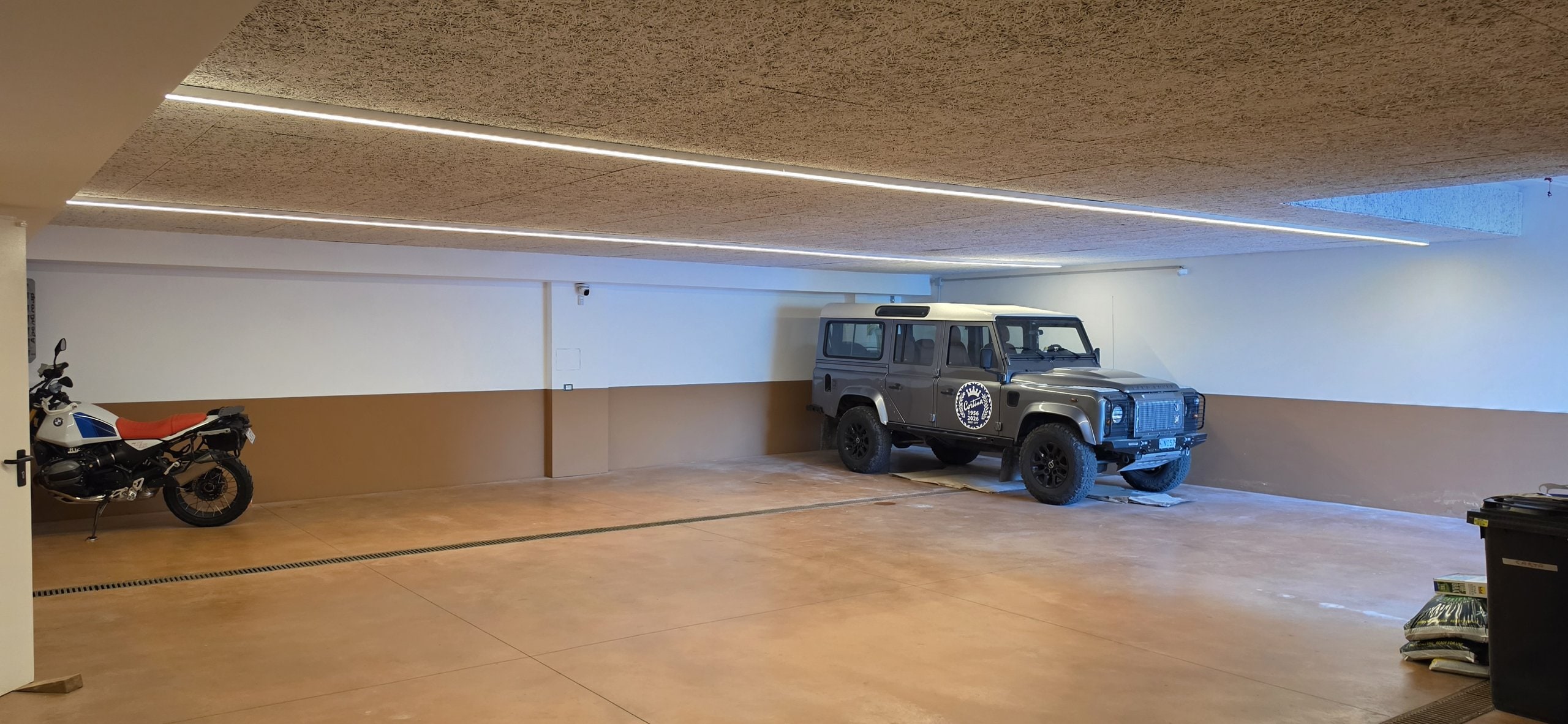 Underground garage of Villa Il Castelletto with a Land Rover Defender parked on the right and a motorcycle on the left, under lit ceiling strips