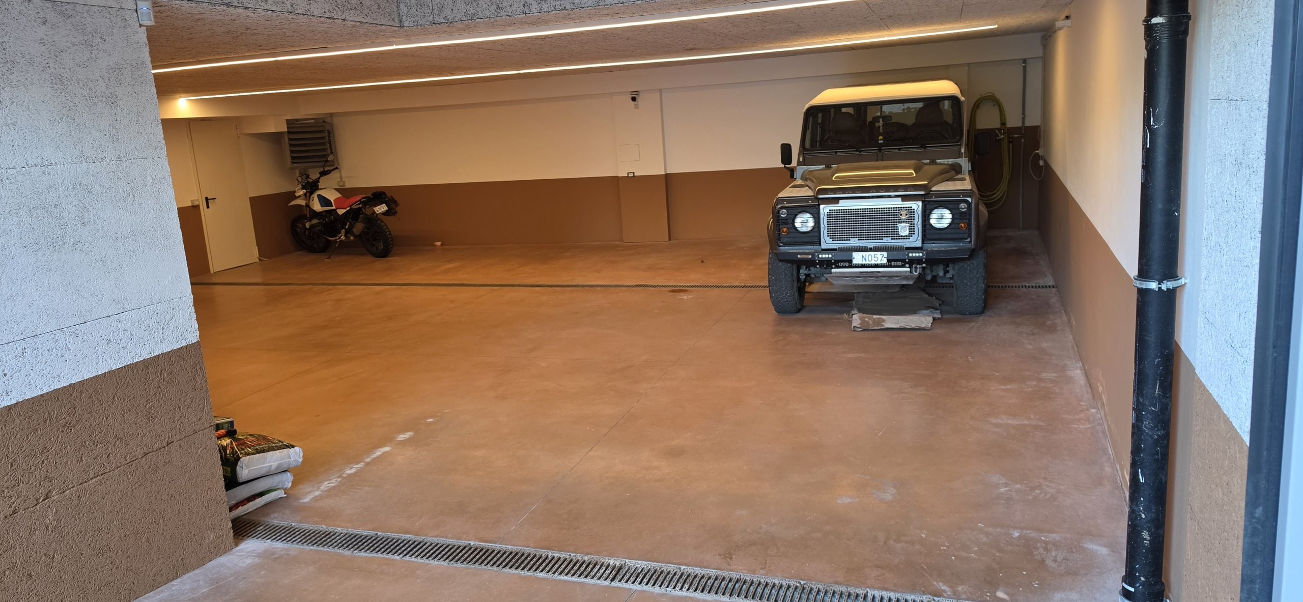 Wide view of the villa's garage from floor level, with a Land Rover Defender and a motorcycle in the parking bays