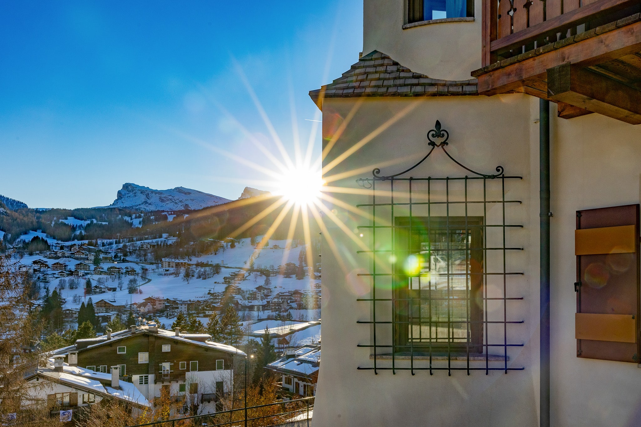 Torretta tirolese di Villa Il Castelletto con finestra a inferriata e targa Cortina 1956–2026, cornice di legno e balcone in luce dorata