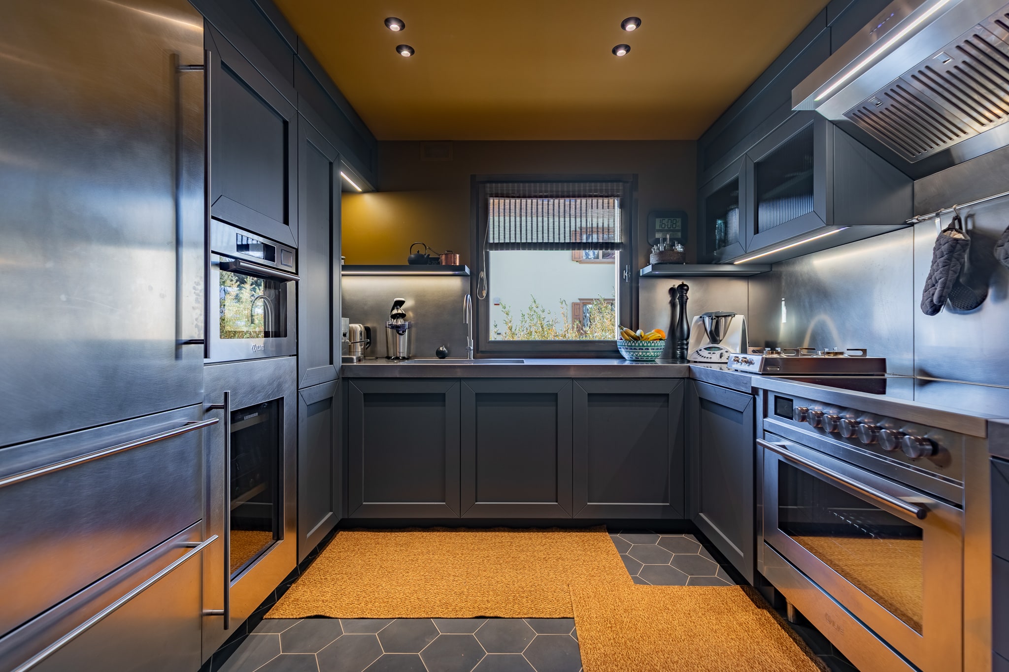 Cucina con mobili scuri, elettrodomestici d'acciaio e soffitto dorato