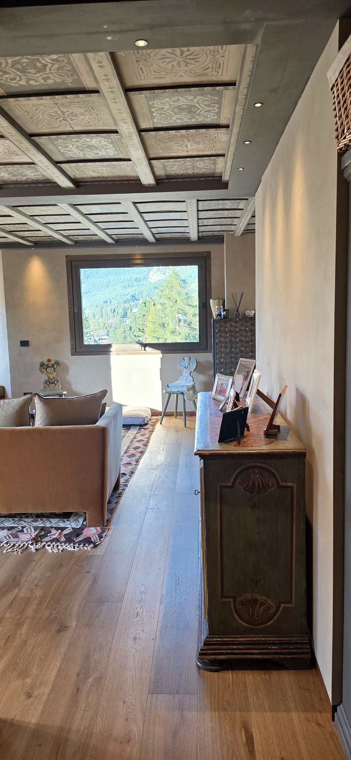 View through to the living room, coffered ceiling, a window onto the mountains and an antique painted cabinet on the wood floor
