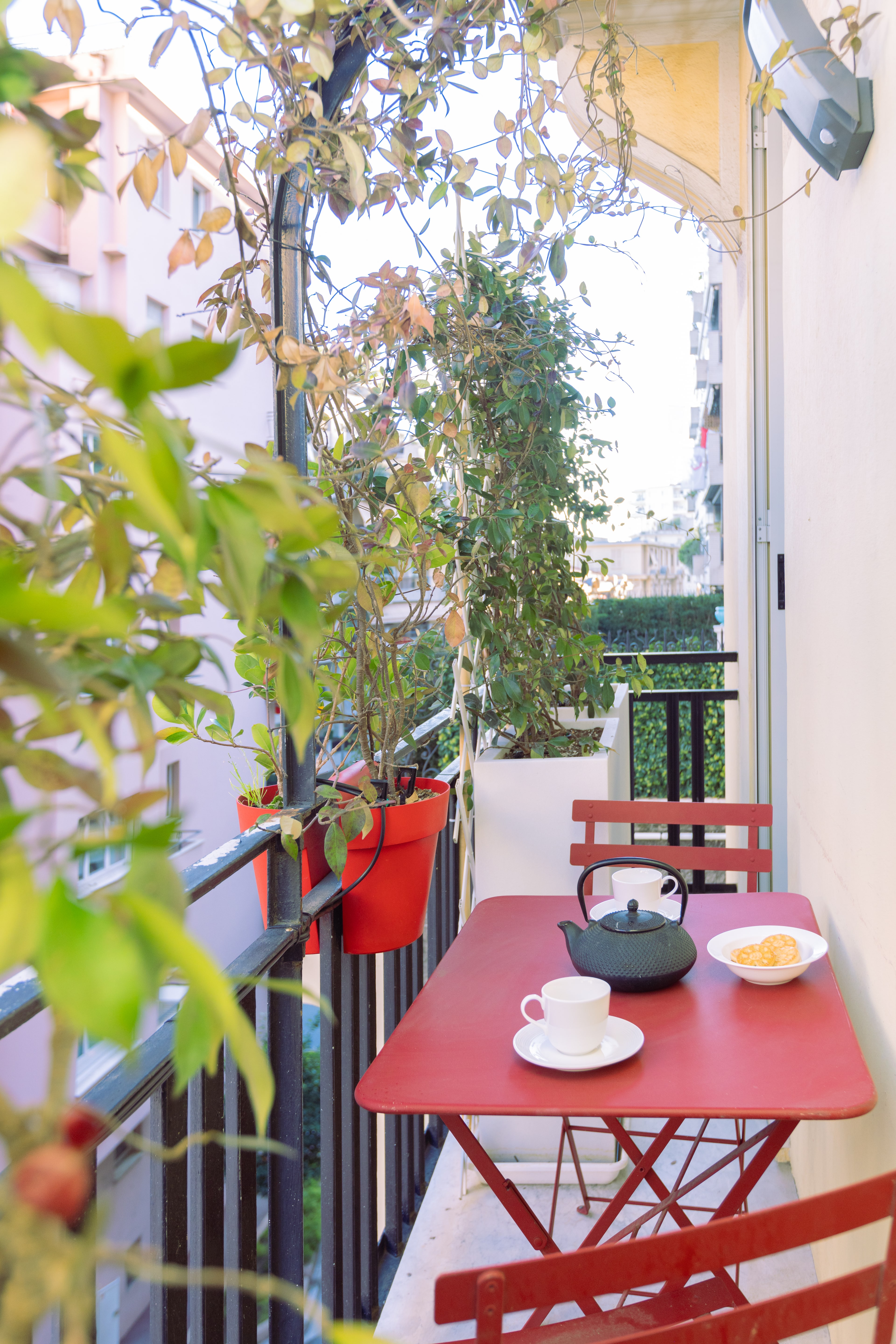 Balconcino con tavolino rosso da bistrot, teiera e tazzina, piante rampicanti