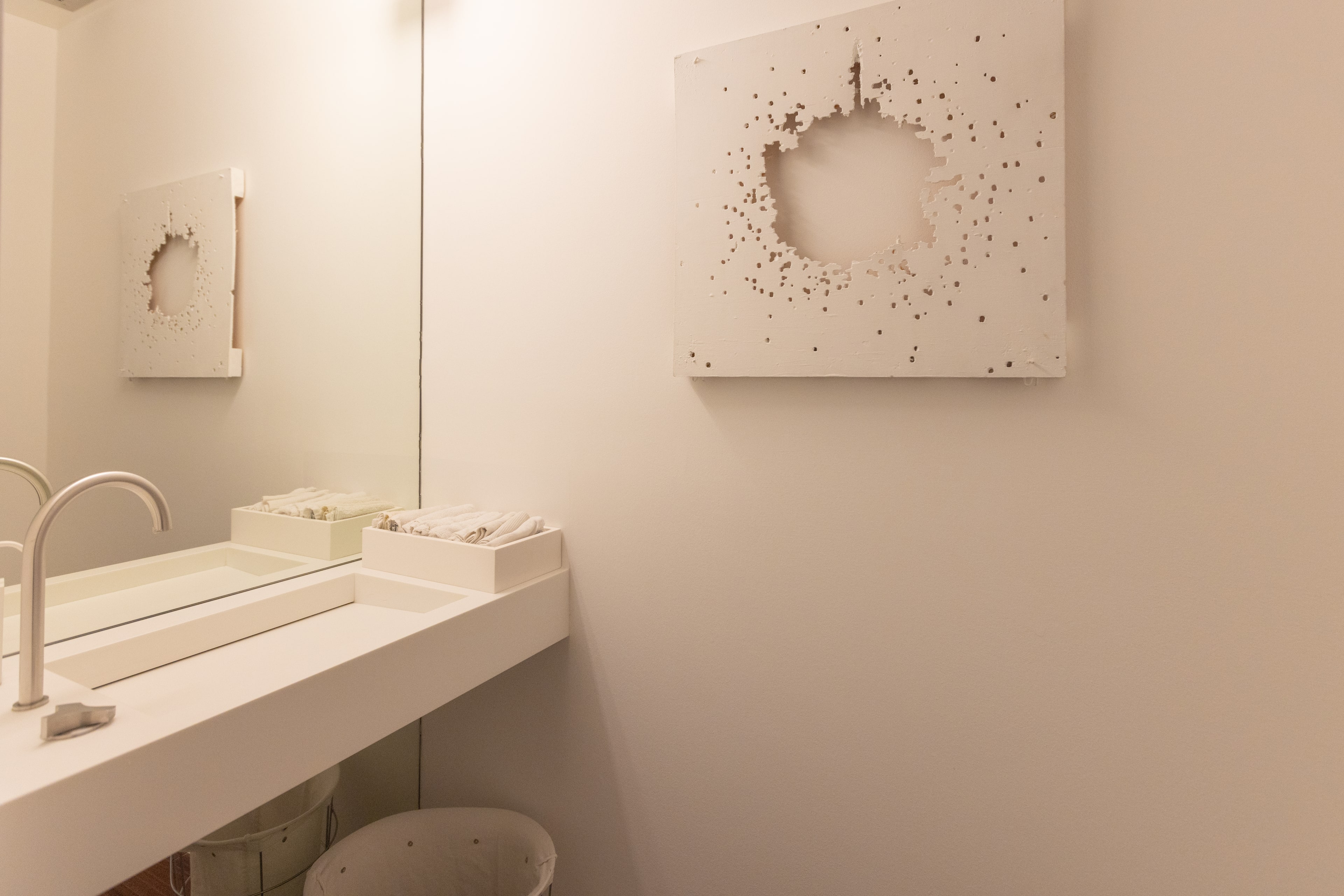 Bagno con opera d'arte traforata bianca, lavabo a canale e mobile a specchio