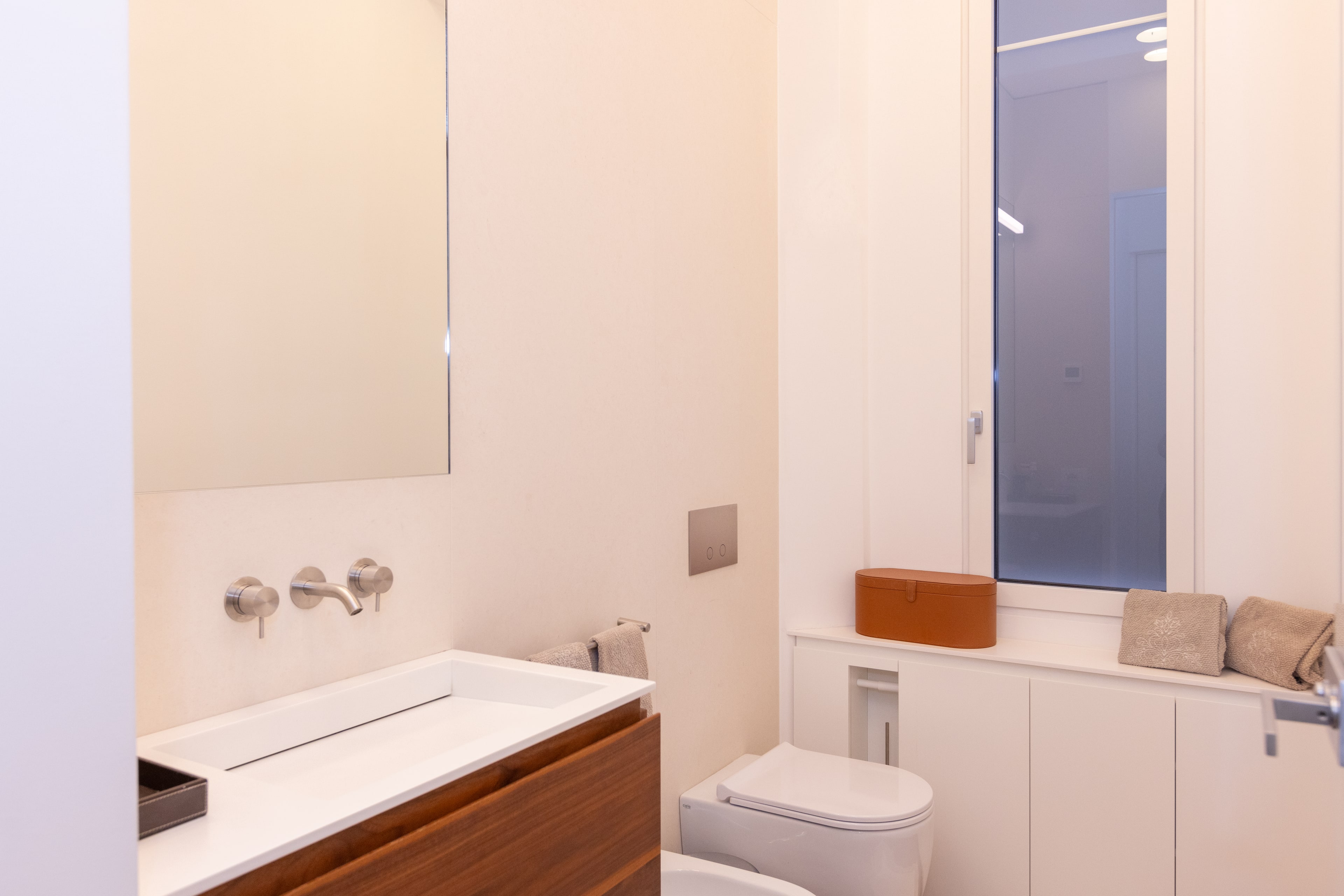 Bagno con mobile lavabo in noce, lavabo bianco e porta in vetro smerigliato