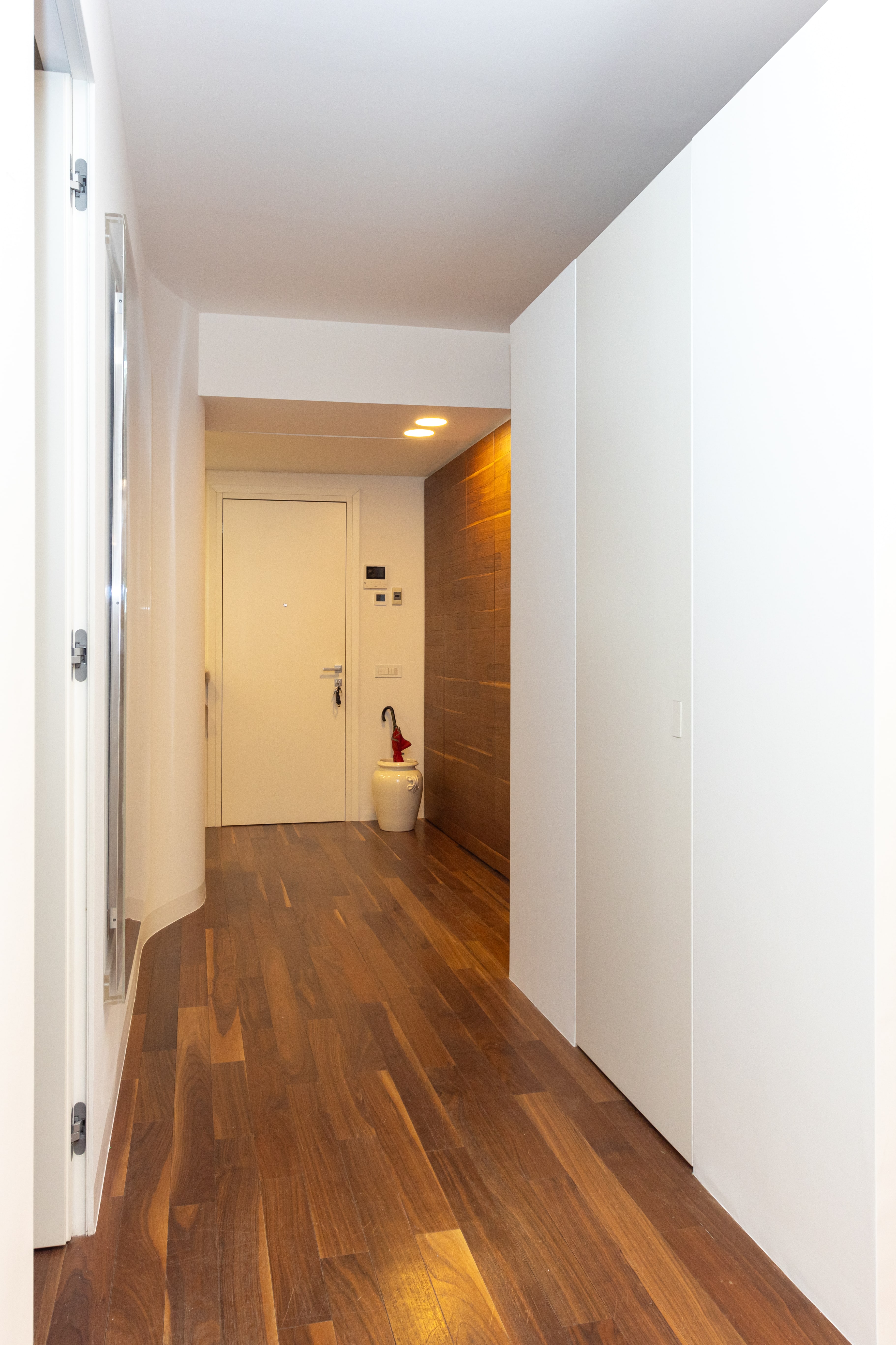 Corridoio d'ingresso con pavimento in noce, parete in legno e vaso bianco accanto alla porta