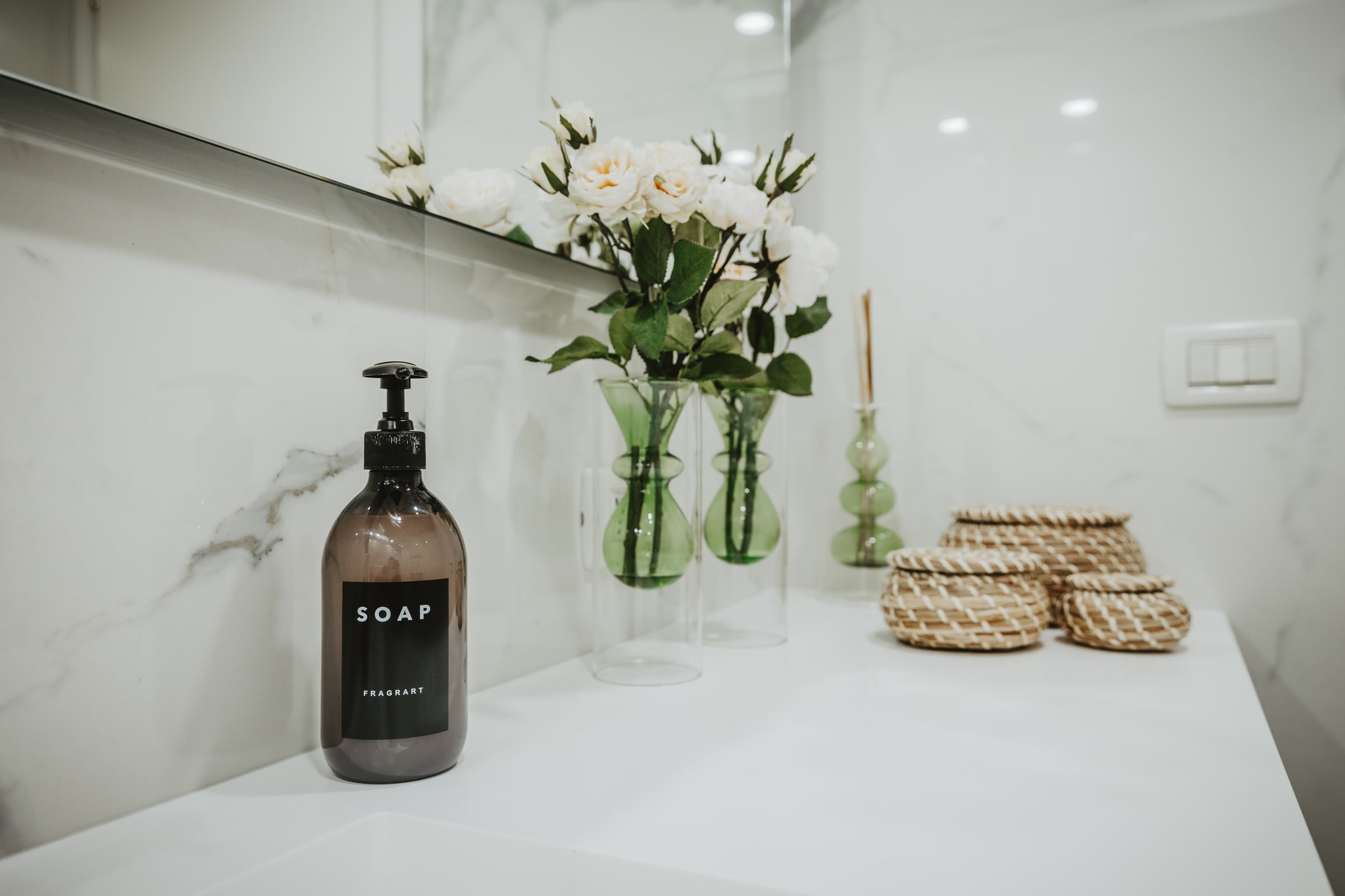 Bagno con pareti in marmo bianco, mobile lavabo scuro e rose fresche