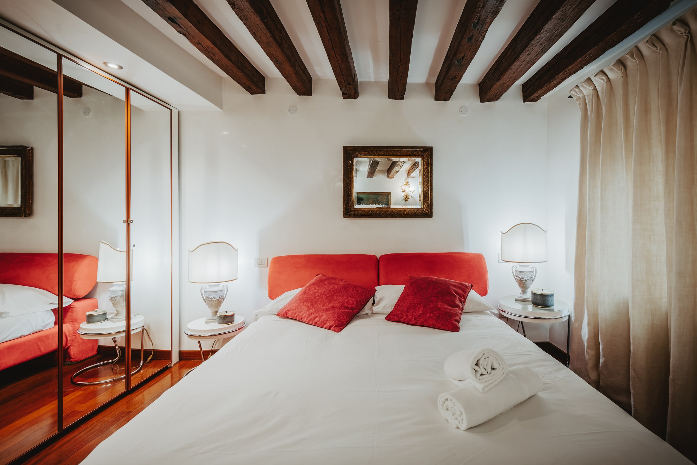 Camera padronale con letto rosso, armadio a specchio e travi