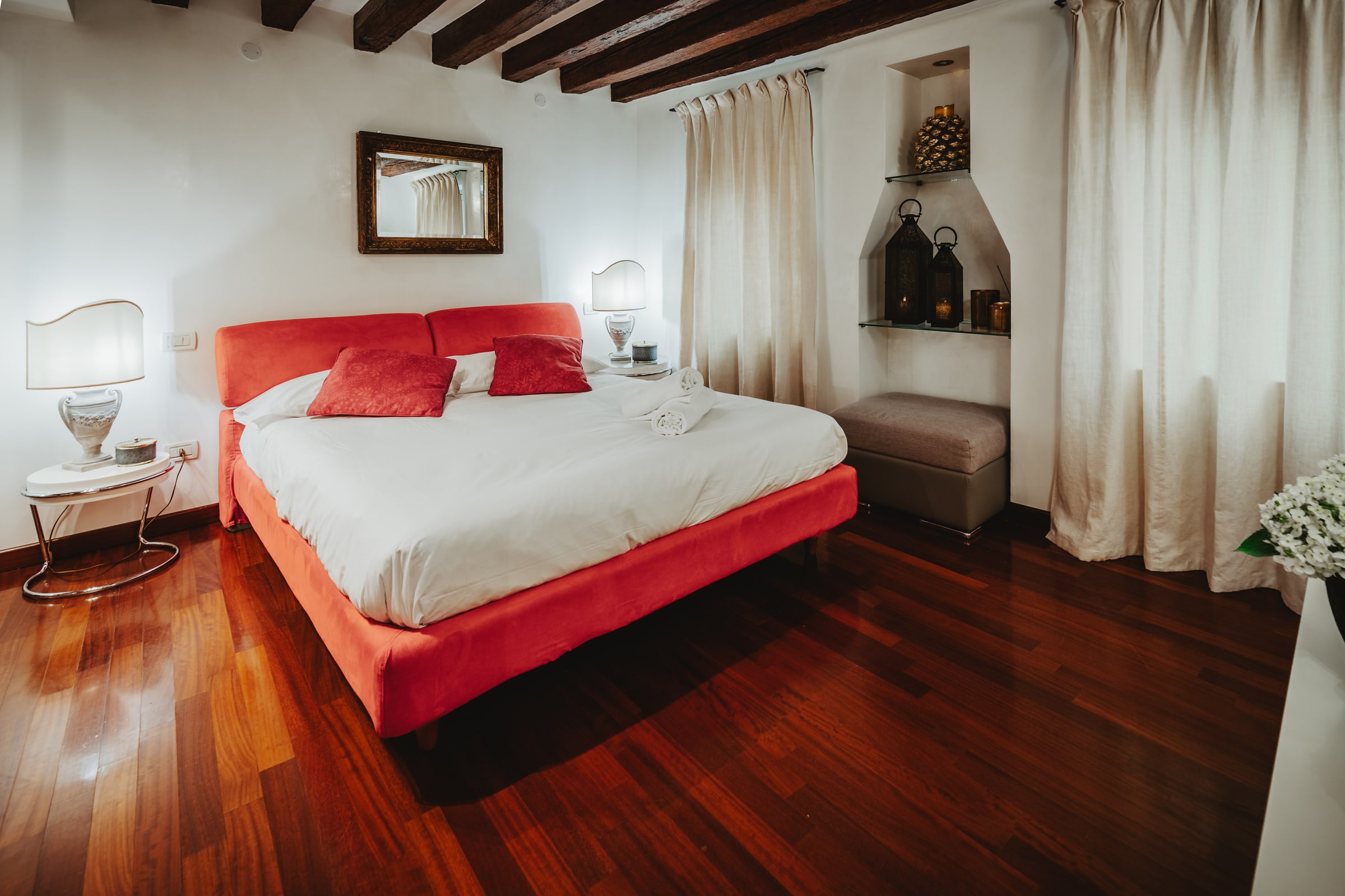 Camera padronale veneziana con letto rosso, specchio dorato e nicchia di pietra