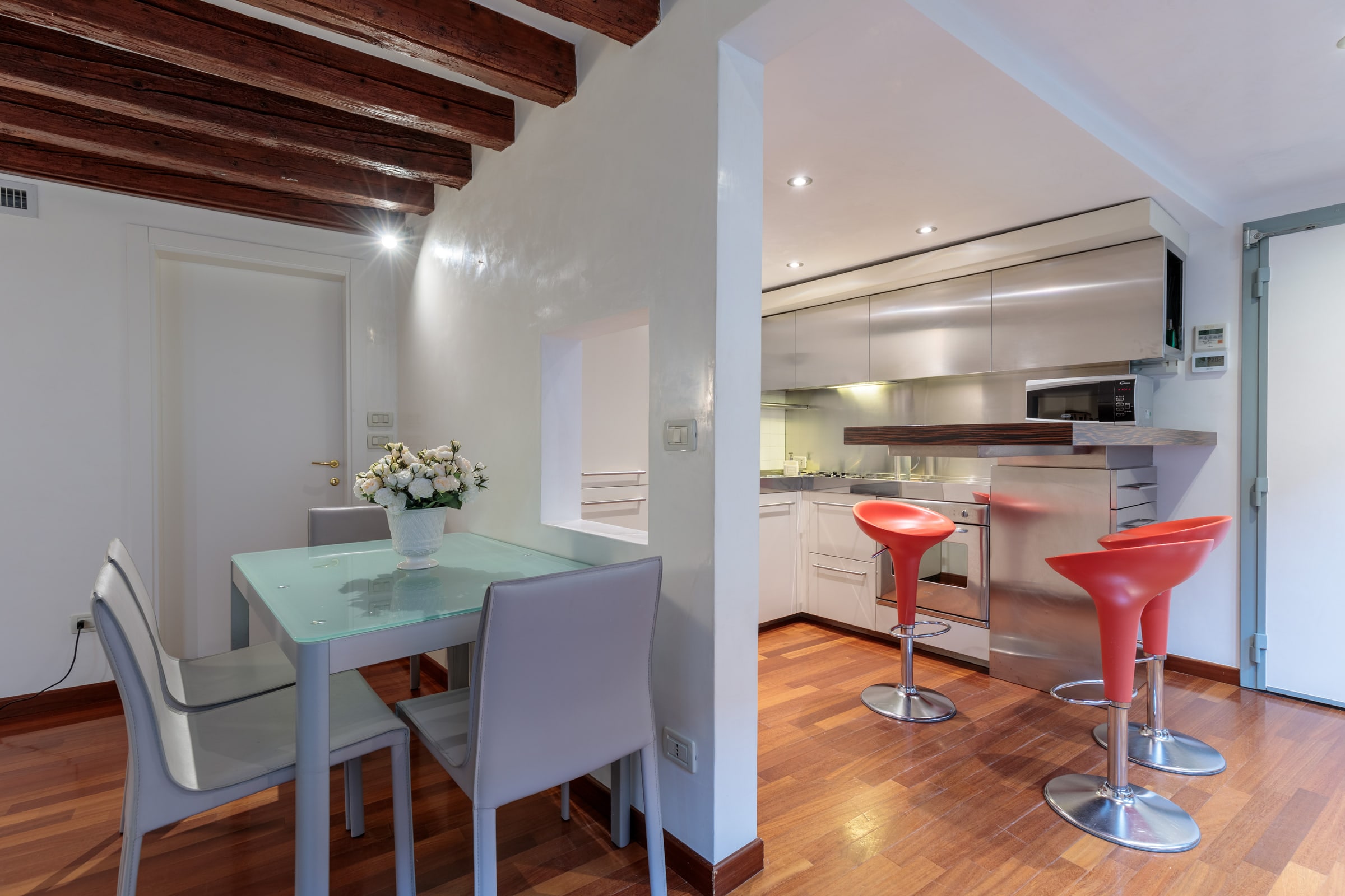 Sala da pranzo con tavolo di vetro, sgabelli rossi da bar e travi a vista
