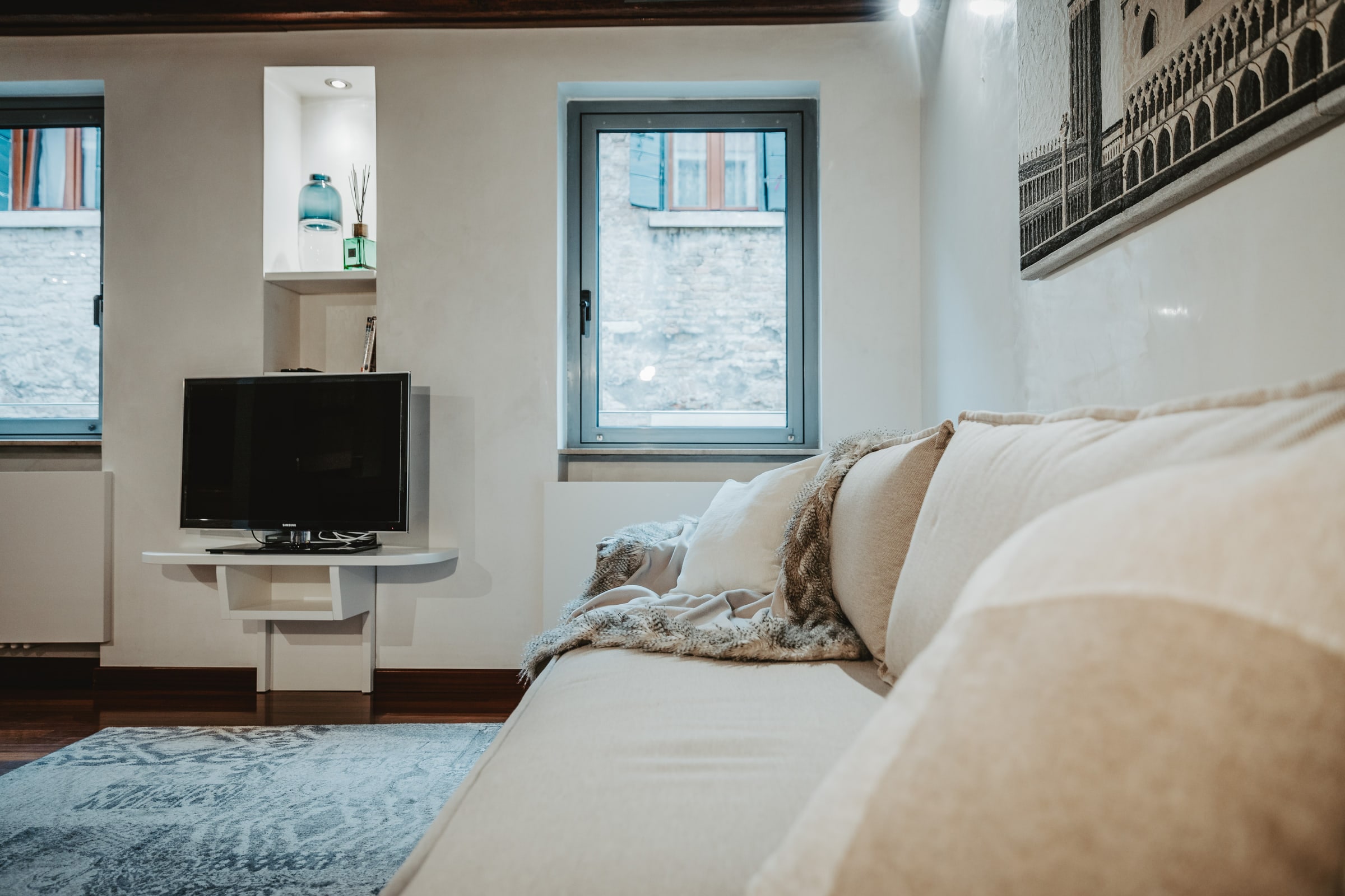 Salotto con nicchia TV, due finestre sulla calle, divano color crema e tappeto blu